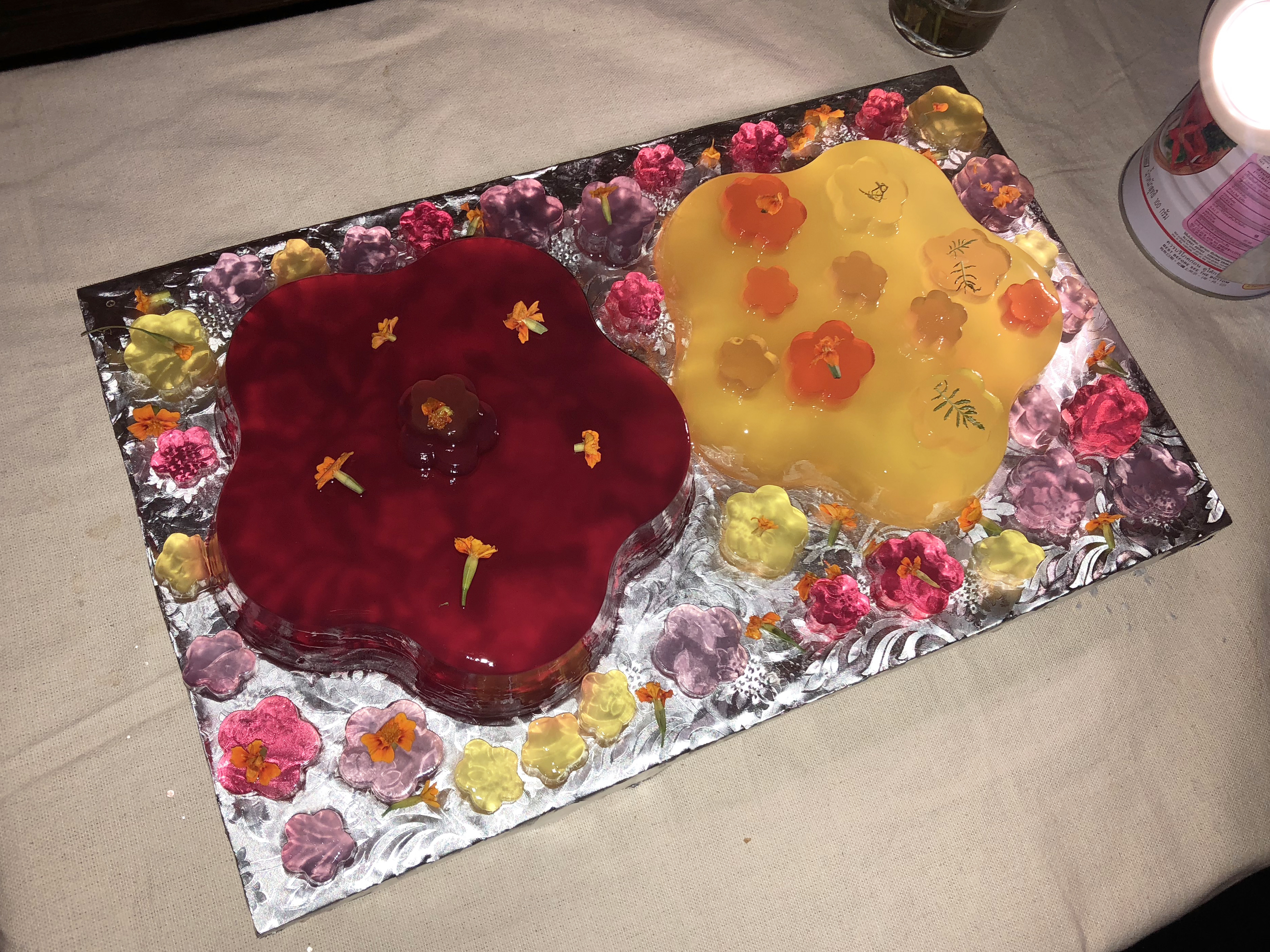 Two brightly colored jello cakes in the shape of flowers on an alliuminium tray